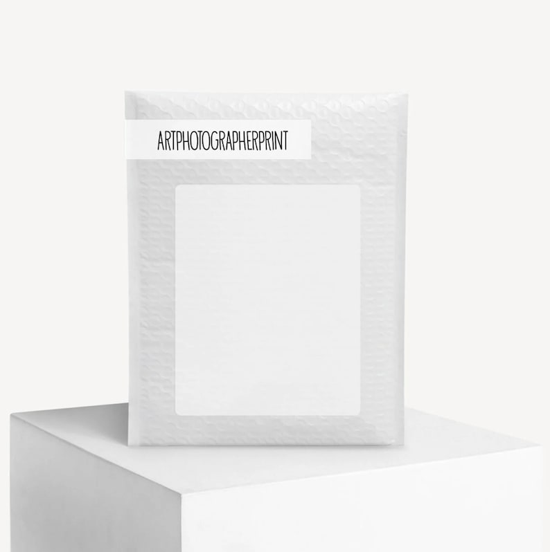 K&ouml;nnte beinhalten: Ein wei&szlig;er Luftpolsterumschlag mit einem rechteckigen Etikett mit der Aufschrift "ARTPHOTOGRAPHERPRINT". Der Umschlag steht auf einem wei&szlig;en W&uuml;rfel.