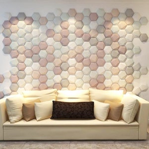 May include: A white couch with multiple pillows in various shades of brown and beige, positioned in front of a wall covered in a geometric pattern of hexagonal tiles in shades of pink, white, and gray.