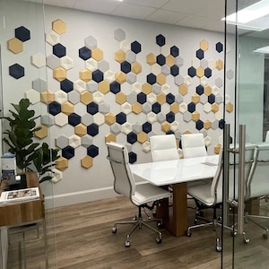 Könnte beinhalten: Ein weißer Konferenztisch mit sechs weißen Stühlen in einem modernen Büro. Die Wand hinter dem Tisch ist mit einem geometrischen Muster aus sechseckigen Fliesen in Gold-, Blau- und Grautönen verziert.