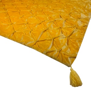 K&ouml;nnte beinhalten: Eine gelbe Samtdecke mit einem gesteppten Muster und einer Quaste.