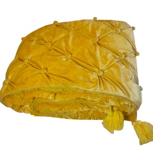 K&ouml;nnte beinhalten: Eine gelbe Samtdecke mit gestepptem Muster und Quasten. Die Decke ist gefaltet und f&uuml;hlt sich weich und luxuri&ouml;s an.