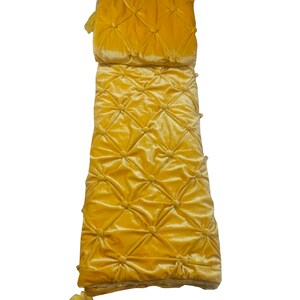 K&ouml;nnte beinhalten: Ein langes, rechteckiges, gelbes Samtkissen mit Knopfkn&ouml;pfen und Quasten an den Enden.