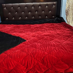 Könnte beinhalten: Ein Bett mit einem braunen Kopfteil mit rautenförmiger Steppung und kristallartigen Knöpfen. Das Bett ist mit einer rot-schwarzen Steppdecke bedeckt. Der rote Teil ist einfarbig, der schwarze Teil ist dreieckig.