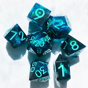 May include: A set of six teal blue dice with green glitter and white numbers. The dice are in various shapes and sizes.