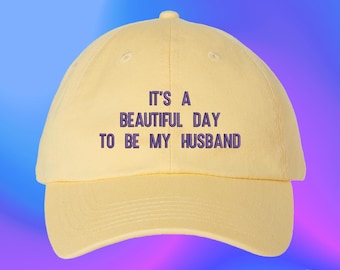 Peut inclure: Une casquette de baseball jaune pâle avec le texte brodé IT'S A BEAUTIFUL DAY TO BE MY HUSBAND en lettres violet foncé. La casquette présente une calotte structurée, une visière incurvée et un bouton au sommet du design à six panneaux.