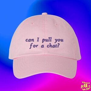 以下が含まれることがあります： 濃い紫色の糸で「can I pull you for a chat?」というテキストが刺繍された、ライトピンクの野球帽。この帽子は、構造化されたクラウン、カーブしたつば、そして上部中央にボタンを備えており、シンプルで清潔感のあるデザインに仕上がっています。