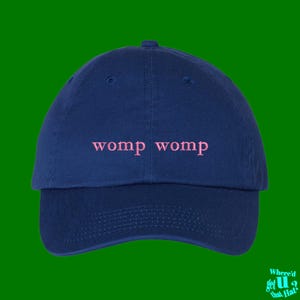 Könnte beinhalten: Eine marineblaue Baseballkappe mit dem Text "womp womp" in rosa gestickt.