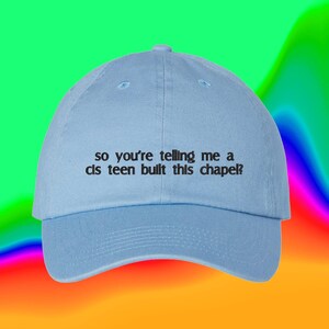 Peut inclure: Une casquette de baseball bleu clair avec une visière incurvée et une sangle réglable à l'arrière. L'avant de la casquette présente un texte brodé en noir qui dit : "so you're telling me a cis teen built this chapel?" en police minuscule.