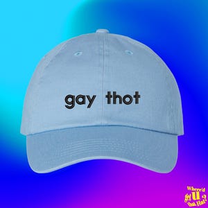 Puede incluir: Una gorra de béisbol de color azul claro con el texto "gay thot" bordado en hilo negro en los paneles frontales. La gorra tiene una corona estructurada, una visera curva y un botón en la parte superior, con un diseño sencillo.