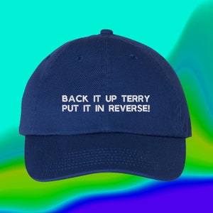 May include: A navy blue baseball cap with white embroidered text that reads "Back it up Terry Put it in reverse!"