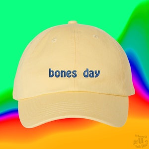 May include: A yellow baseball cap with the text "bones day" embroidered in blue on the front.
