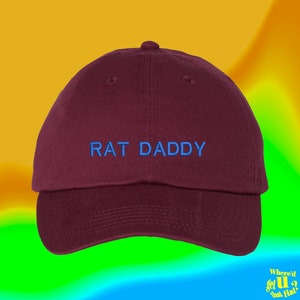 Könnte beinhalten: Eine marineblaue Baseballkappe mit dem Schriftzug "RAT DADDY" in blauer Stickerei.