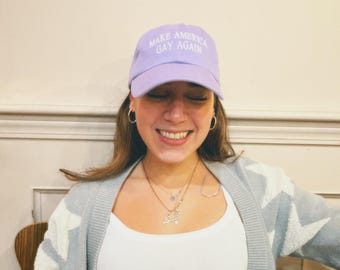 Può includere: Un cappellino da baseball color viola chiaro con il testo MAKE AMERICA GAY AGAIN ricamato in bianco sul pannello frontale. Il cappellino presenta una visiera curva e una corona strutturata, realizzata in tessuto tinta unita con cuciture.