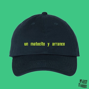 Può includere: Un cappello da baseball blu scuro con il testo "un mate­cito y arranco" ricamato in giallo.