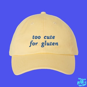 Könnte beinhalten: Eine gelbe Baseballkappe mit dem Text "too cute for gluten", der in Blau gestickt ist.