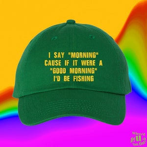 以下が含まれることがあります： 黄色の刺繍で「I say "morning" cause if it were a "good morning" I'd be fishing.」と書かれた緑色のベースボールキャップ