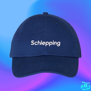以下が含まれることがあります： 前面に白い刺繍で「Schlepping」と書かれたネイビーブルーのベースボールキャップ