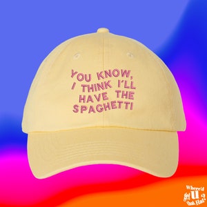 May include: A yellow baseball cap with a pink embroidered phrase that reads "YOU KNOW, I THINK I'LL HAVE THE SPAGHETTI".