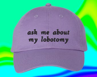 May include: A light purple baseball cap featuring the embroidered black text "ask me about my lobotomy" centered on the front panel. The cap has a structured crown, a curved brim, and a button at the top, showcasing a simple and clean design.