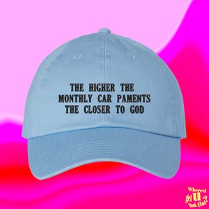 Puede incluir: Una gorra de béisbol azul claro con el texto "THE HIGHER THE MONTHLY CAR PAMENTS THE CLOSER TO GOD" bordado en negro.