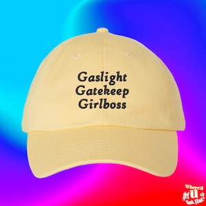 Peut inclure: Une casquette de baseball jaune avec du texte brodé en noir qui dit "Gaslight Gatekeep Girlboss".