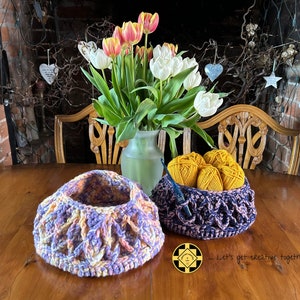 May include: Two crocheted baskets, one purple and pink, the other dark purple and black, filled with yellow yarn balls. A vase of white and orange tulips sits on a wooden table with the text "...Let's get creative together!"