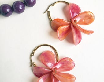 May include: A pair of gold hoop earrings with pink and orange flower-shaped charms. The charms are made of translucent plastic with a marbled effect.