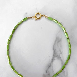 May include: A green and gold beaded necklace with a gold clasp. The necklace is made of small, rectangular green beads and small, round gold beads.