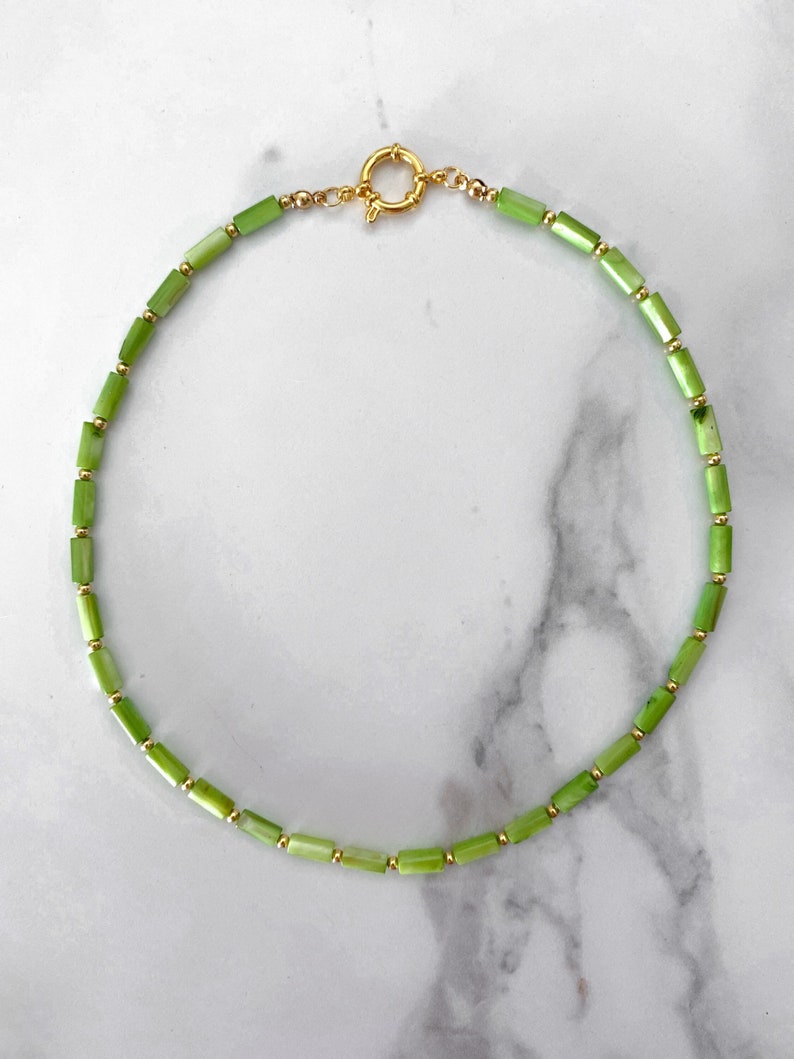 May include: A green and gold beaded necklace with a gold clasp. The necklace is made of small, rectangular green beads and small, round gold beads.