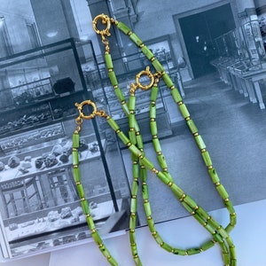 May include: A double strand necklace made of green and white rectangular beads with gold accents. The necklace has a gold clasp.