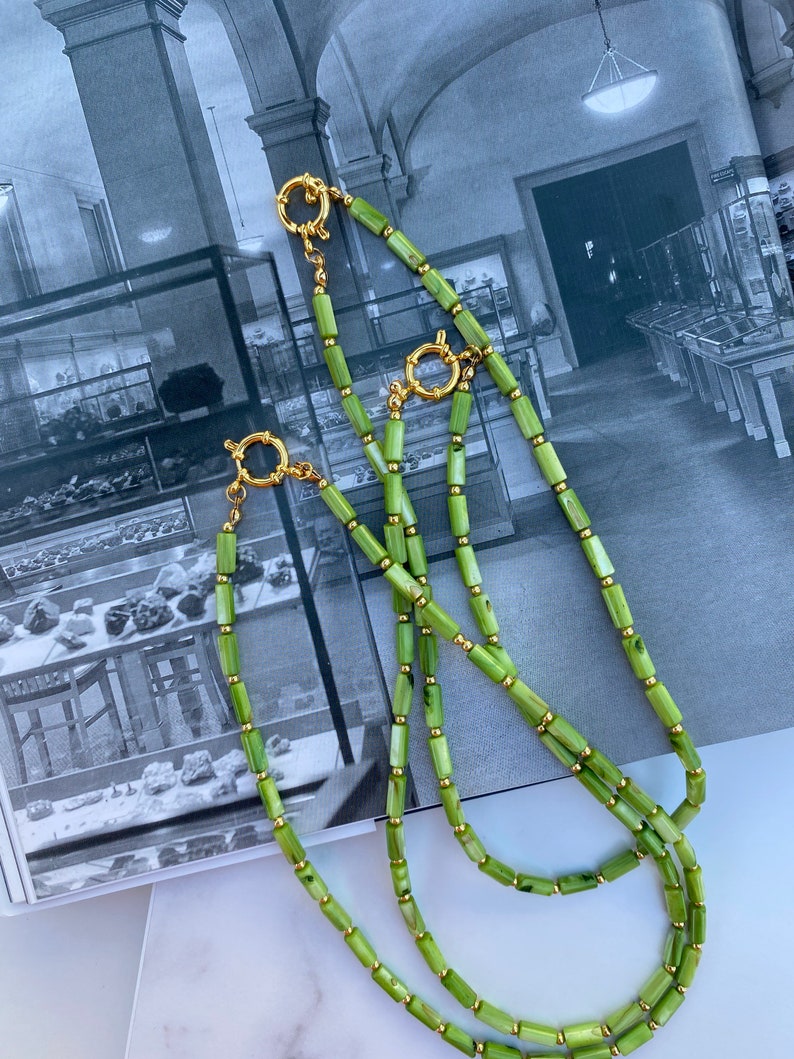 May include: A double strand necklace made of green and white rectangular beads with gold accents. The necklace has a gold clasp.