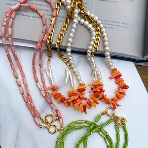 May include: Three necklaces with gold clasps. The top necklace is made of white pearls. The middle necklace is made of pink and orange coral. The bottom necklace is made of green jade.
