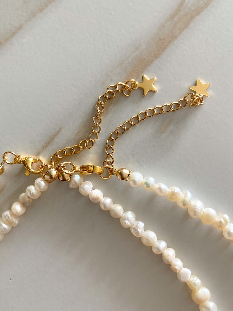 Pu&ograve; includere: Una delicata collana di perle con catena dorata e dettagli a forma di stella. La collana presenta piccole perle bianche di forma irregolare e una chiusura dorata. La catena &egrave; regolabile.