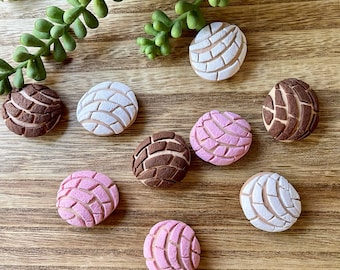 May include: Eight colorful, round, decorative ornaments with a raised, textured design. The ornaments are in shades of brown, pink, and white. They are arranged on a wooden surface.