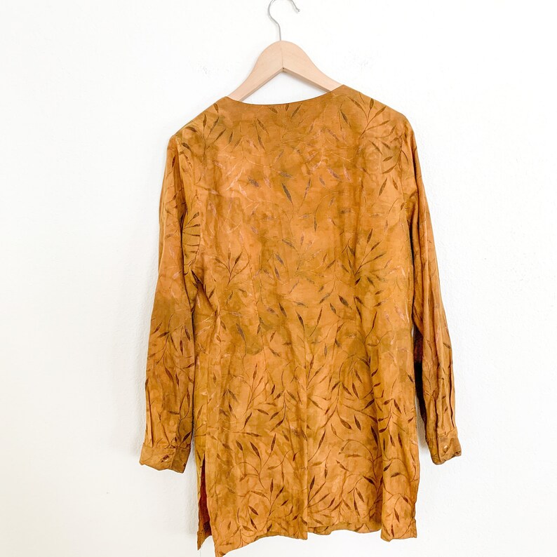 May include: A long-sleeved, mustard yellow tunic with a leaf pattern. The tunic has a V-neck and a relaxed fit.