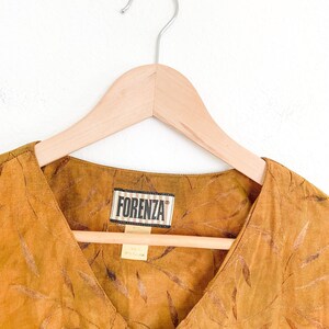 May include: A brown, sleeveless top with a V-neckline and a leaf pattern. The top has a label that reads "Forenza" in black text.