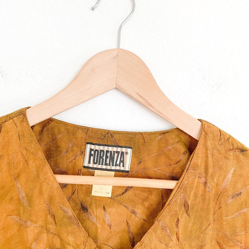May include: A brown, sleeveless top with a V-neckline and a leaf pattern. The top has a label that reads "Forenza" in black text.