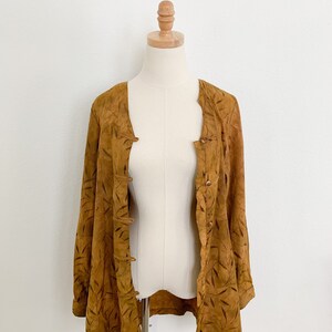 May include: A brown suede jacket with a leaf pattern. The jacket has a button-up front and long sleeves.