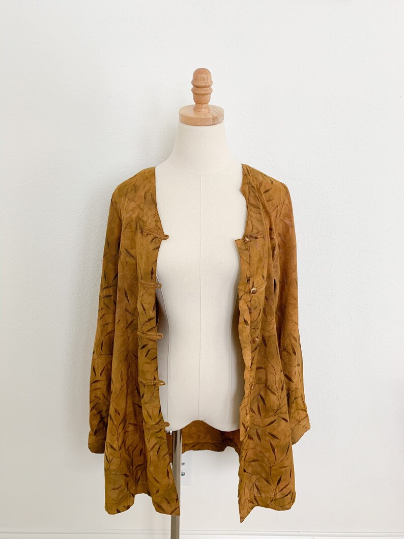 May include: A brown suede jacket with a leaf pattern. The jacket has a button-up front and long sleeves.