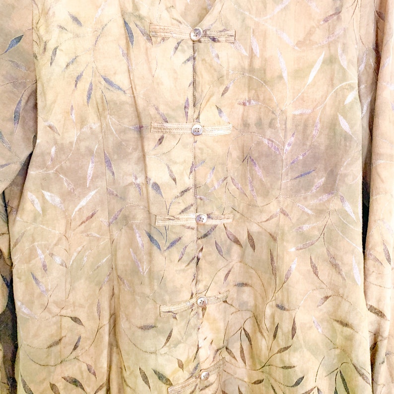 May include: A beige button-up shirt with a leaf pattern. The shirt has a mandarin collar and five buttons down the front.