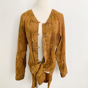 May include: A long-sleeved, brown suede jacket with a leaf pattern and a tie closure. The jacket has a mandarin collar and a button closure.