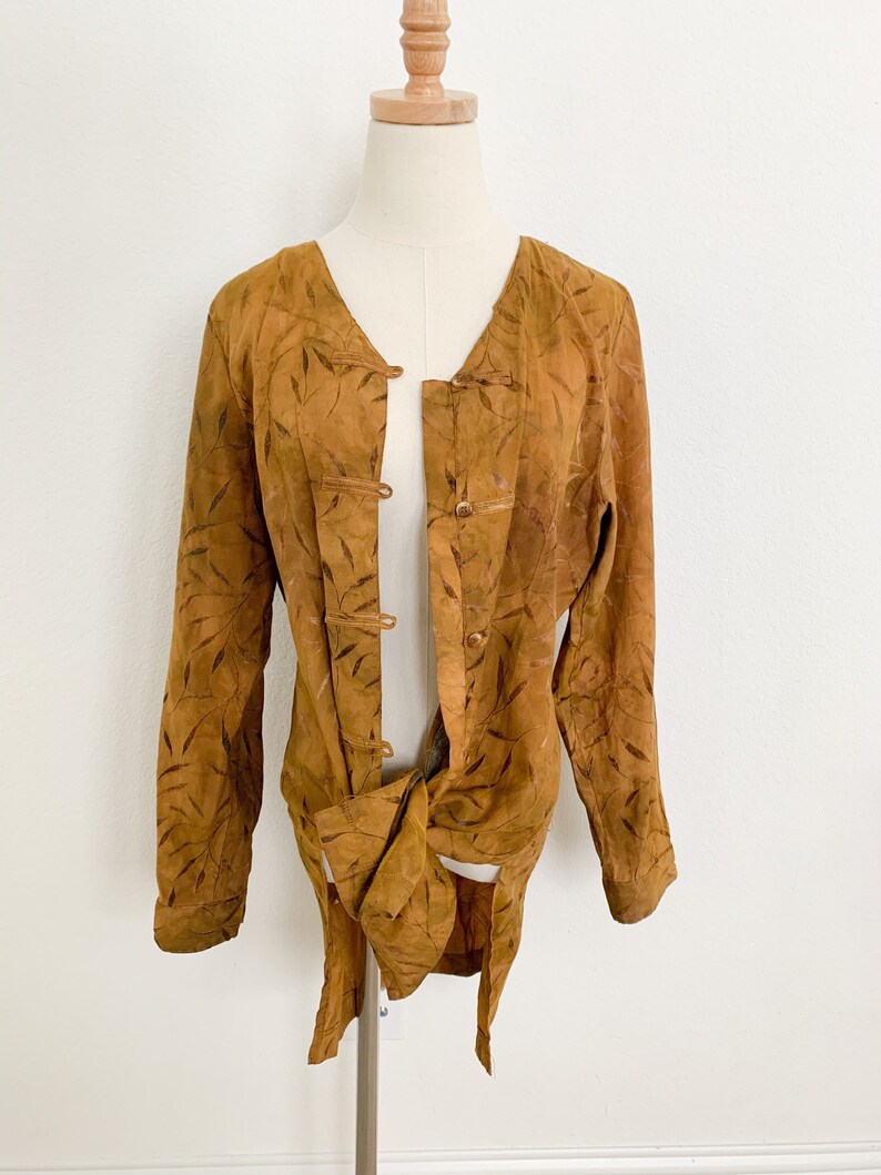 May include: A long-sleeved, brown suede jacket with a leaf pattern and a tie closure. The jacket has a mandarin collar and a button closure.