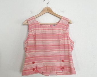 Pode incluir: Uma blusa sem mangas de listras rosa e brancas com decote redondo e três botões de cada lado. A blusa está pendurada em um cabide de madeira.