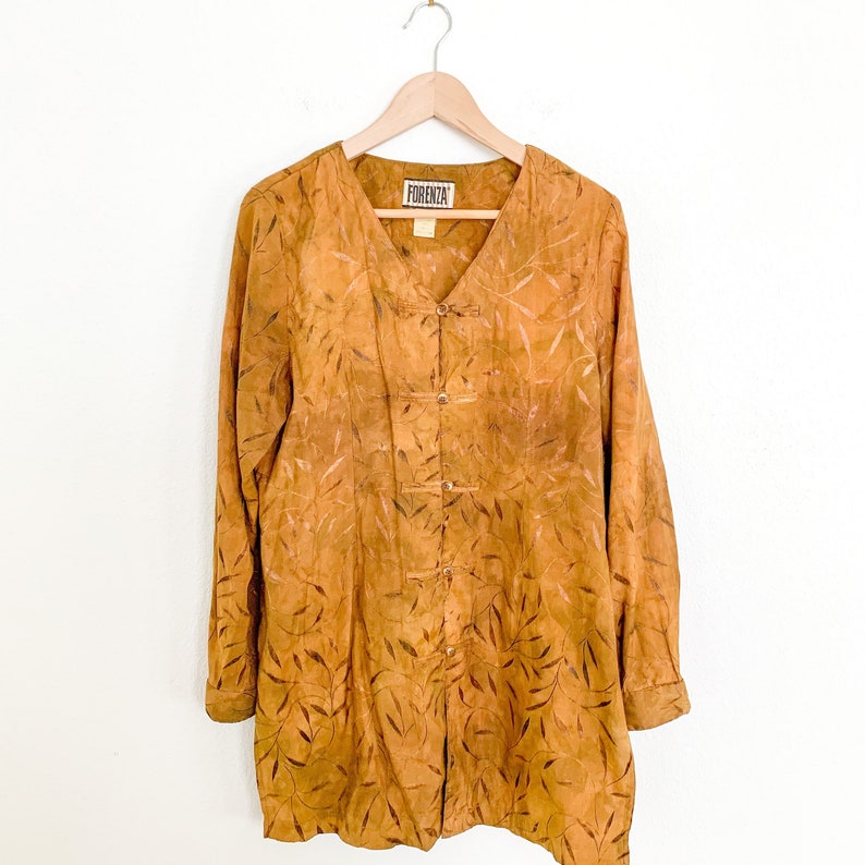 May include: A long-sleeved, mustard yellow button-up shirt with a leaf pattern. The shirt has a mandarin collar and a label that reads "Florenza".