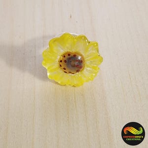 May include: A yellow glass ring with a red and brown center, resembling a sunflower.