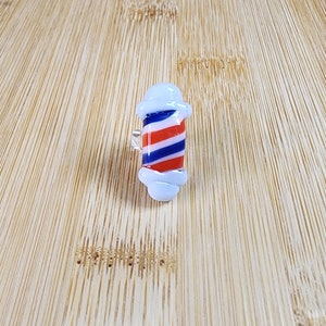 May include: A white glass ring with a red, white, and blue barber pole design.