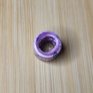 May include: A purple ceramic ring with a white center and black speckles.