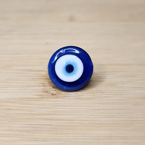 May include: A blue and white evil eye charm with a white pupil and a blue ring around it.