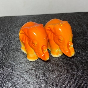 Puede incluir: Dos saleros y pimenteros de cerámica naranja en forma de elefante. Los elefantes se miran con la trompa hacia abajo.