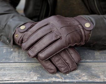 May include: A pair of brown leather gloves with a textured surface. The gloves have a button closure at the wrist.